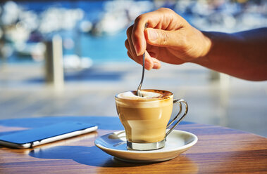 Close-up of woman's hand stirring glass of Espresso Macchiato - DIKF00292