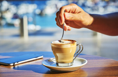 Nahaufnahme der Hand einer Frau, die ein Glas Espresso Macchiato umrührt - DIKF00292