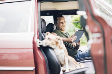 Portrait of smiling man with tablet in car with dog on passenger seat - MOEF00151