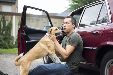 Mann sitzt neben dem Auto und spielt mit seinem Hund, lizenzfreies Stockfoto