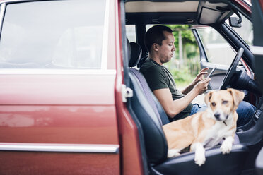 Mann benutzt Tablet im Auto mit Hund auf dem Beifahrersitz - MOEF00157