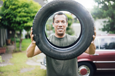 Porträt eines lächelnden Mannes, der einen Autoreifen hält, lizenzfreies Stockfoto