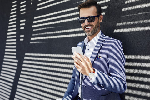 Businessman wearing sunglasses using phone near concrete wall stock photo