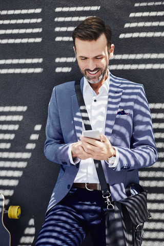 Portrait of businessman with longboard and phone near concrete wall stock photo