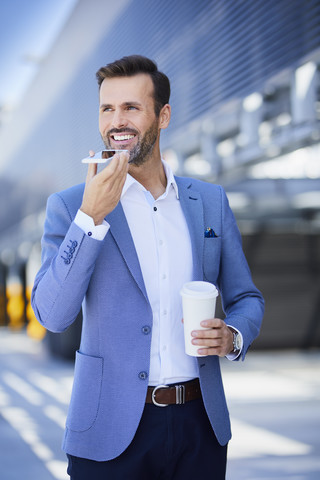 Porträt eines lächelnden Geschäftsmannes mit Telefon und Kaffee in der Stadt, lizenzfreies Stockfoto