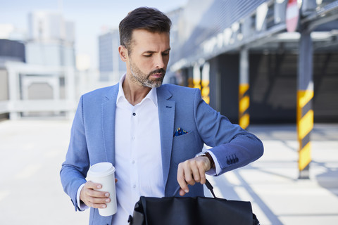 Geschäftsmann prüft die Zeit und hält einen Kaffee im Freien, lizenzfreies Stockfoto