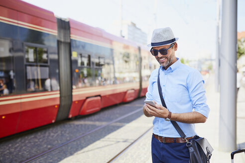 Reisende in der Stadt, die an der Straßenbahnhaltestelle ein Handy benutzen - BSZF00028