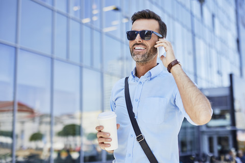 Fröhlicher Geschäftsmann telefoniert und hält Kaffee im Freien, lizenzfreies Stockfoto