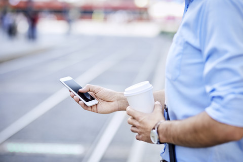 Close-up of businessman using phone and holding coffee outdoors stock photo