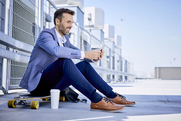 Businessman sitting on longboard and using phone - BSZF00043