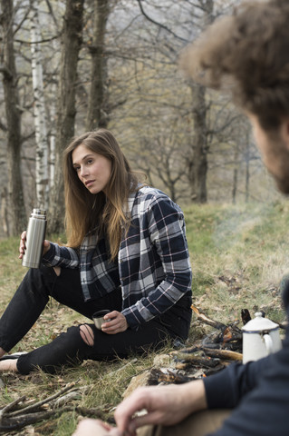 Frau mit Thermoskanne am Lagerfeuer im Wald, lizenzfreies Stockfoto