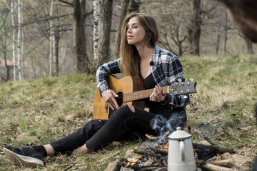 Woman playing guitar in forest at campfire - ZOCF00511