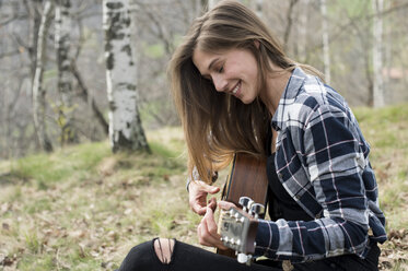 Smiling woman playing guitar in forest - ZOCF00512