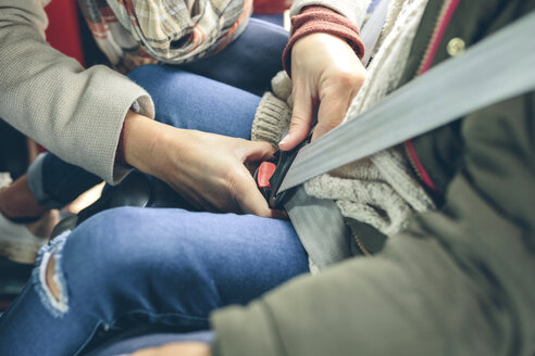 Close-up of woman fastening safety seat belt of girl sitting in a car - DAPF00808