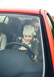 Little girl with wool cap driving car sitting on father's lap - DAPF00815