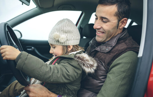 Happy little girl with wool cap driving car sitting on father's lap - DAPF00816