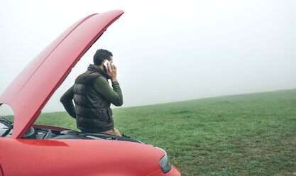 Man talking on cell phone next to broken car - DAPF00820