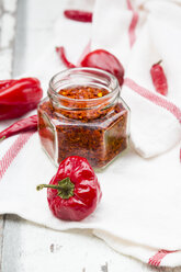 Glass of chili flakes and red chili pods on kitchen towel - LVF06307