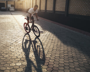 Junger Mann fährt Fixie-Bike im Hinterhof bei Sonnenuntergang - VPIF00184