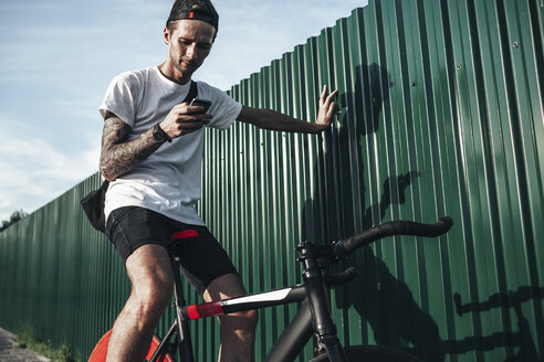 Young man using cell phone on fixie bike - VPIF00187