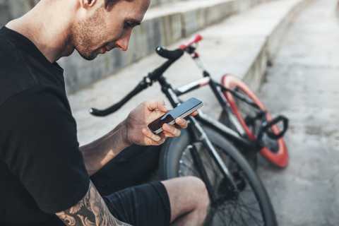 Young man sitting next to fixie bike using cell phone stock photo