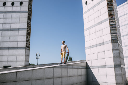 Junger Mann mit Longboard umgeben von moderner Architektur - VPIF00205