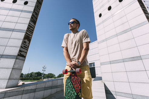 Junger Mann mit Longboard umgeben von moderner Architektur - VPIF00209