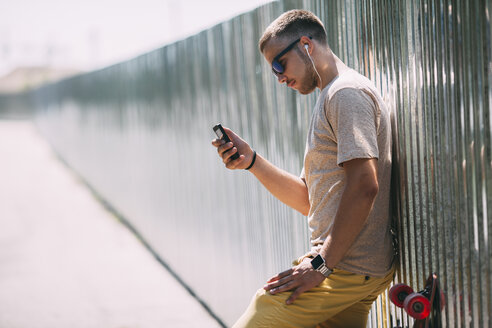 Junger Mann mit Handy und Kopfhörern an eine Wand gelehnt - VPIF00220