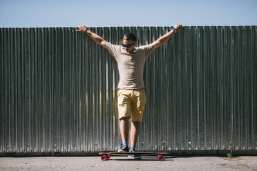 Junger Mann mit Longboard an einer Wand stehend - VPIF00227