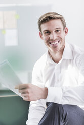 Portrait of smiling businessman in office holding documents - UUF11835