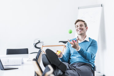 Lächelnder Geschäftsmann, der im Büro mit Bällen jongliert - UUF11840