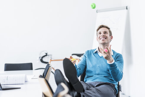 Smiling businessman juggling with balls in office - UUF11841