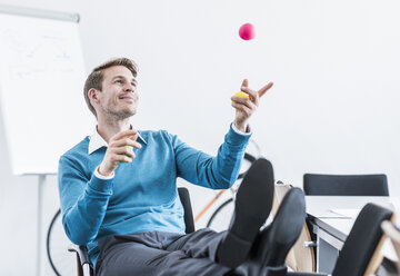 Smiling businessman juggling with balls in office - UUF11842