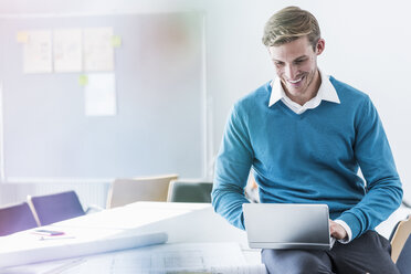 Smiling businessman using mini laptop in office - UUF11845