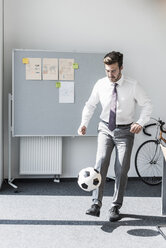 Businessman playing football in office - UUF11850