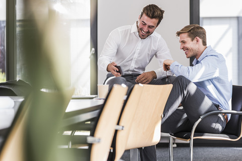 Zwei glückliche Kollegen im Büro, die gemeinsam ein Handy benutzen, lizenzfreies Stockfoto