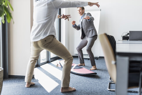 Two playful colleagues with surfboard in office - UUF11875