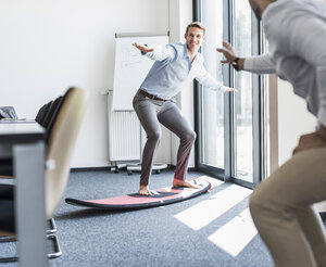 Two playful colleagues with surfboard in office - UUF11876