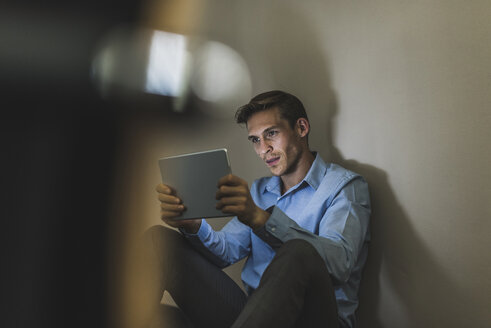 Businessman sitting on the floor using tablet - UUF11879