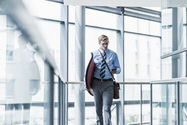 Businessman with cell phone carrying surfboard in office - UUF11883