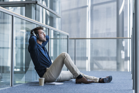 Geschäftsmann mit Kopfhörern sitzt auf dem Boden und entspannt sich, lizenzfreies Stockfoto