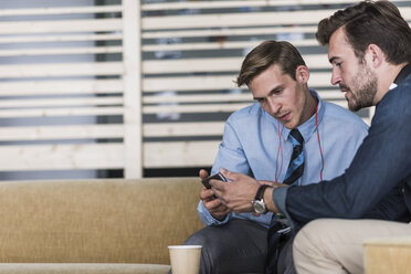 Zwei Kollegen teilen sich ein Mobiltelefon in der Bürolounge - UUF11895