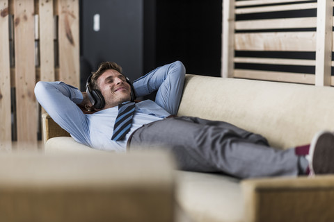 Businessman with headphones lying on couch in office lounge stock photo