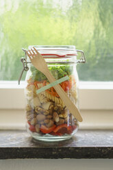 Preserving jar of vegan mixed salad with tofu and pasta on window sill - ECF01893