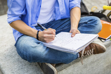 Junger Mann sitzt auf einer Bank und schreibt auf einem Notizblock, Teilansicht - MGIF00141