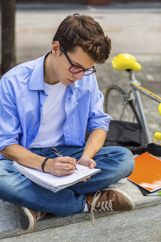 Junger Mann mit Rennrad sitzt auf einer Bank und schreibt auf einem Notizblock, lizenzfreies Stockfoto