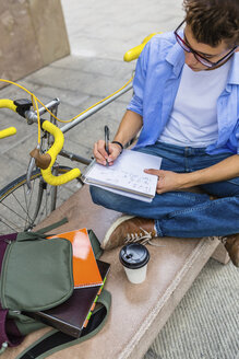 Junger Mann mit Rennrad sitzt auf einer Bank und schreibt auf einem Notizblock - MGIF00149