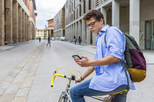 Junger Mann auf dem Rennrad schaut auf sein Handy - MGIF00155