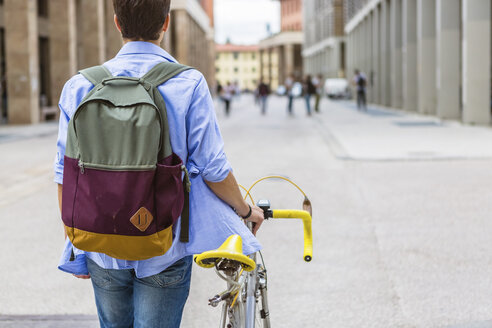 Rückenansicht eines jungen Mannes mit Rucksack, der sein Fahrrad schiebt - MGIF00161