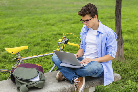 Young man with racing cycle sitting on a bench using laptop stock photo